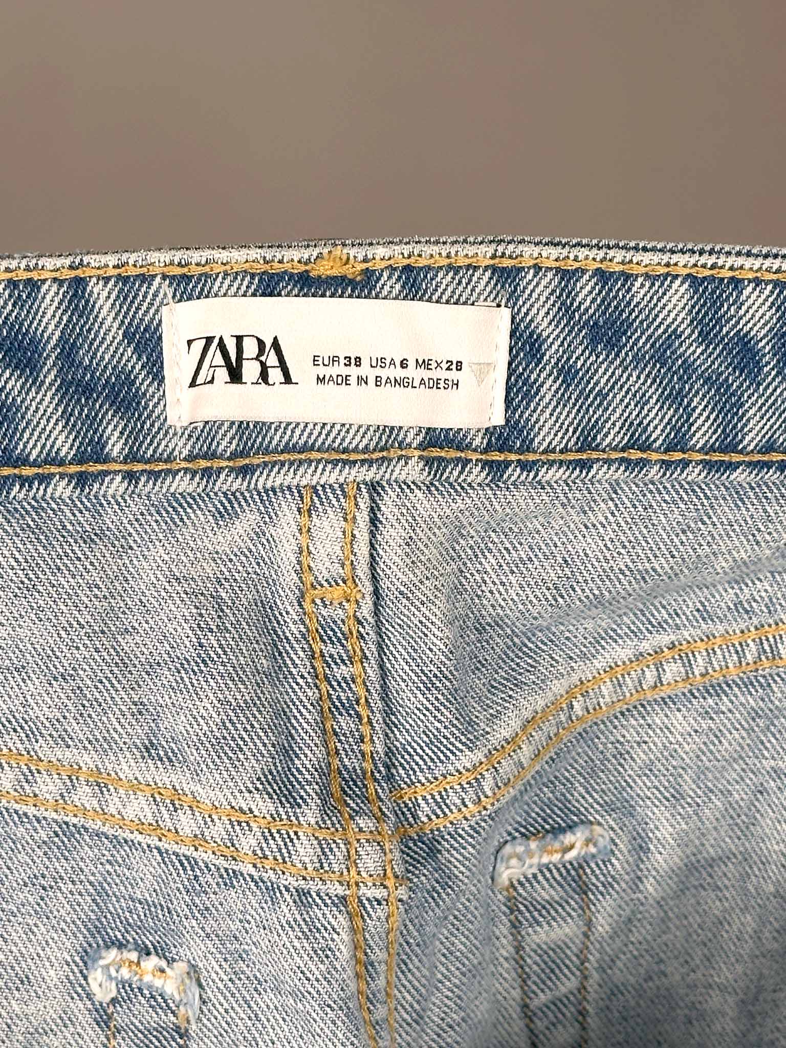 Close-up of a Zara label on a pair of blue jeans with a blurred background.