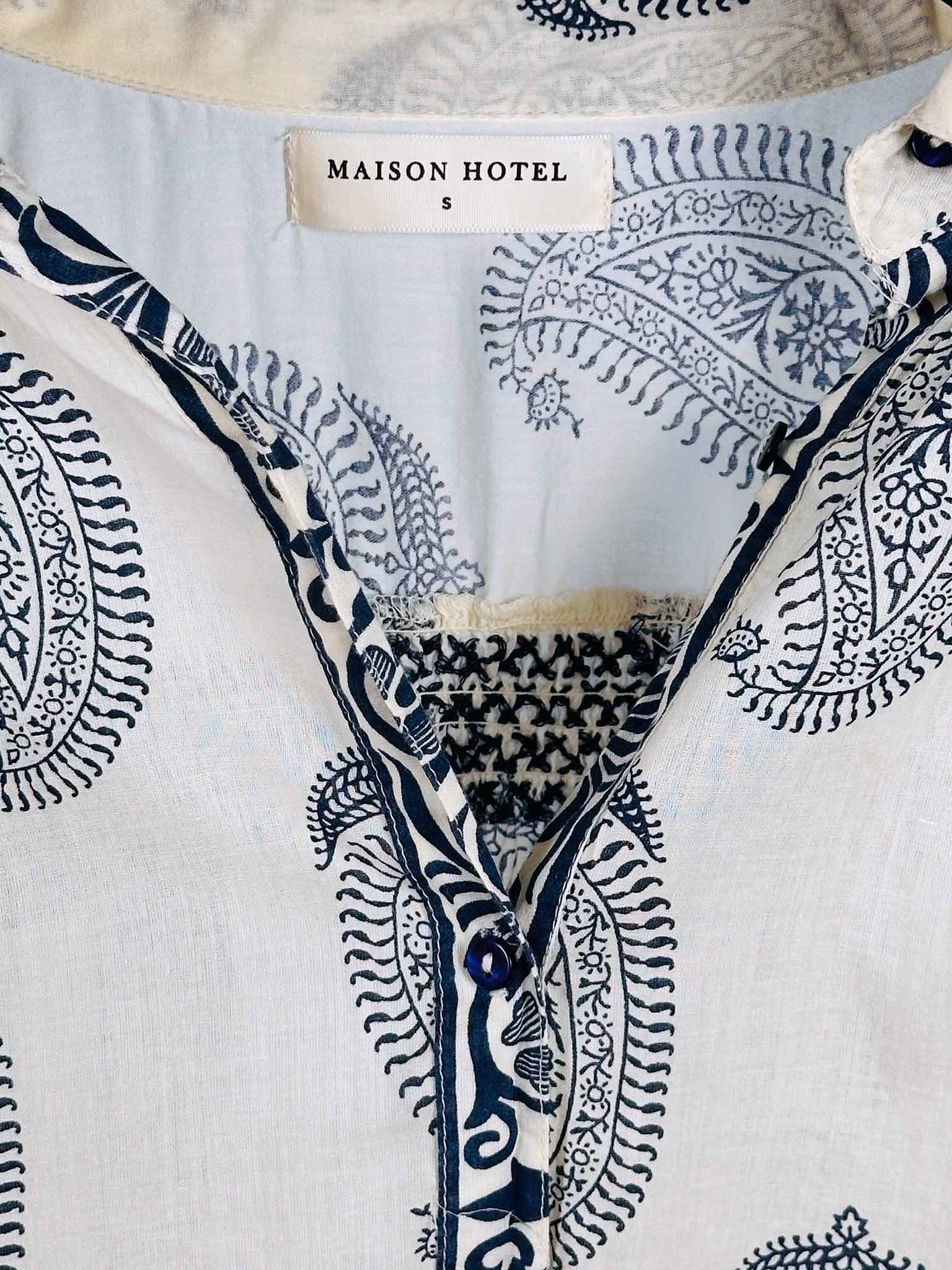 Close-up of a shirt with black patterns and 'MAISON HOTEL' label on a light background
