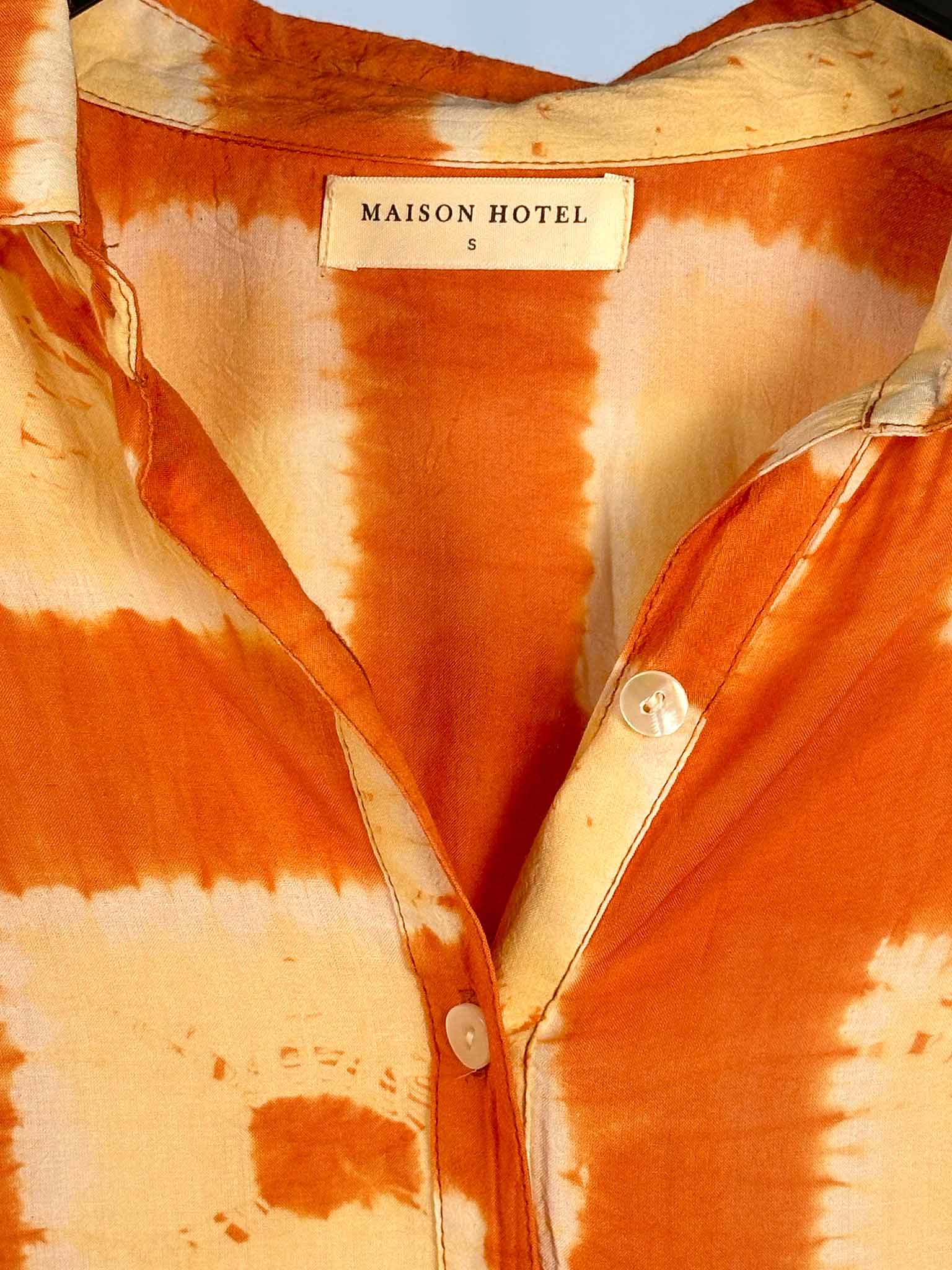 Close-up of a tie-dye shirt with 'Maison Hotel' label on a blurred background