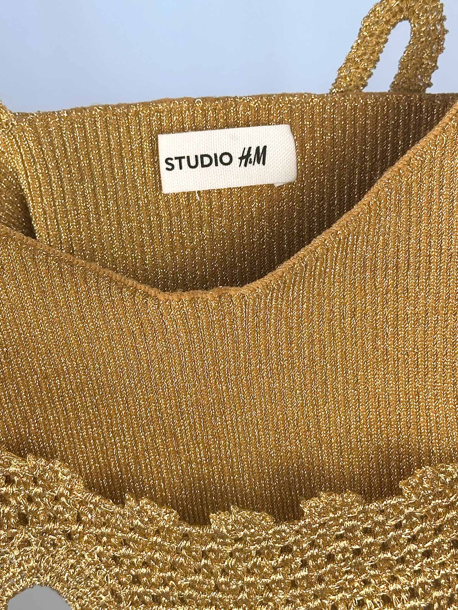 Gold glittery top with 'Studio H&M' label against a blue background