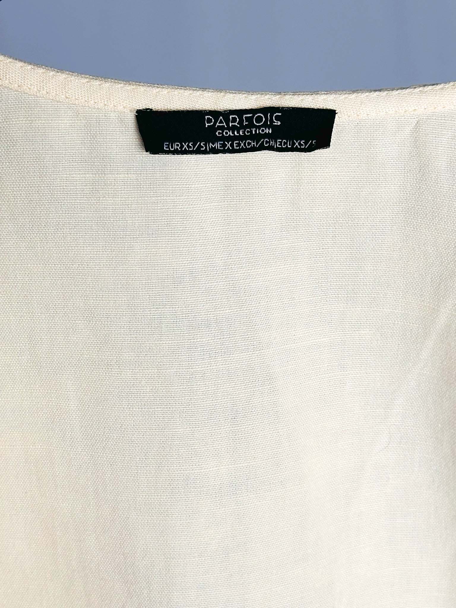 Close-up of a white garment with a Parfois Collection label against a blue background