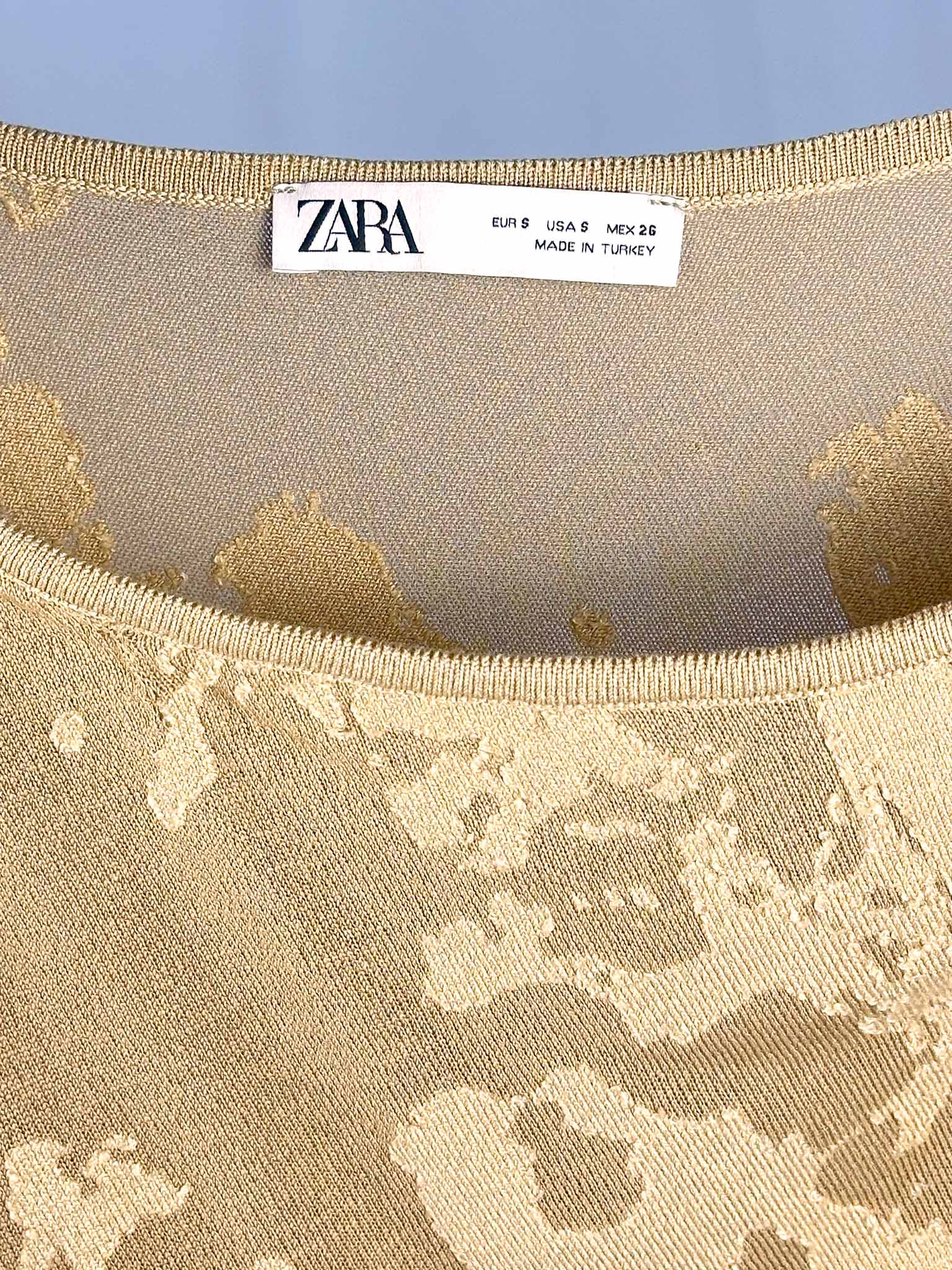 Close-up of Zara label on a beige fabric with gold pattern