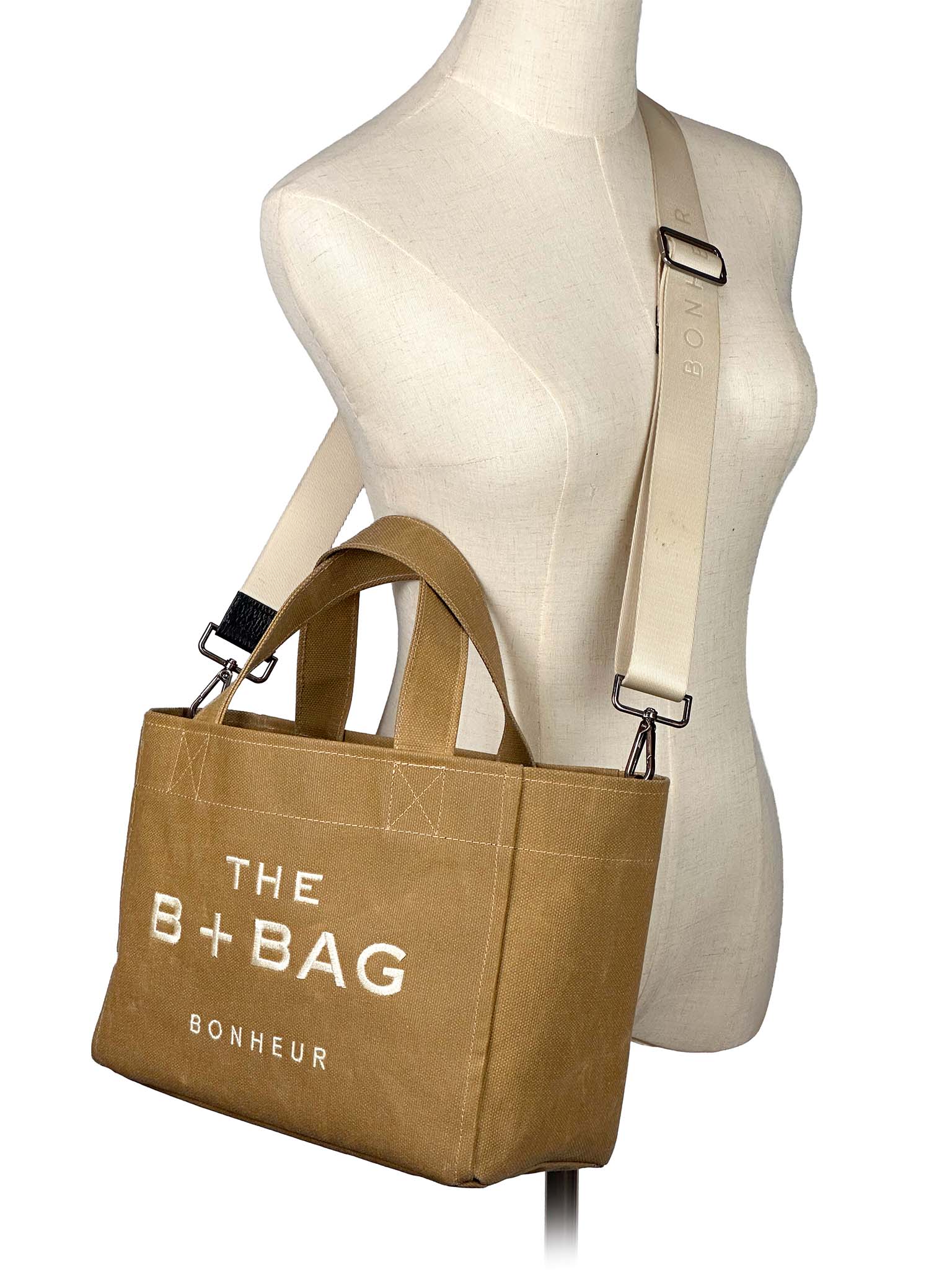 Brown tote bag with 'THE B+BAG BONHEUR' text on a mannequin against a white background