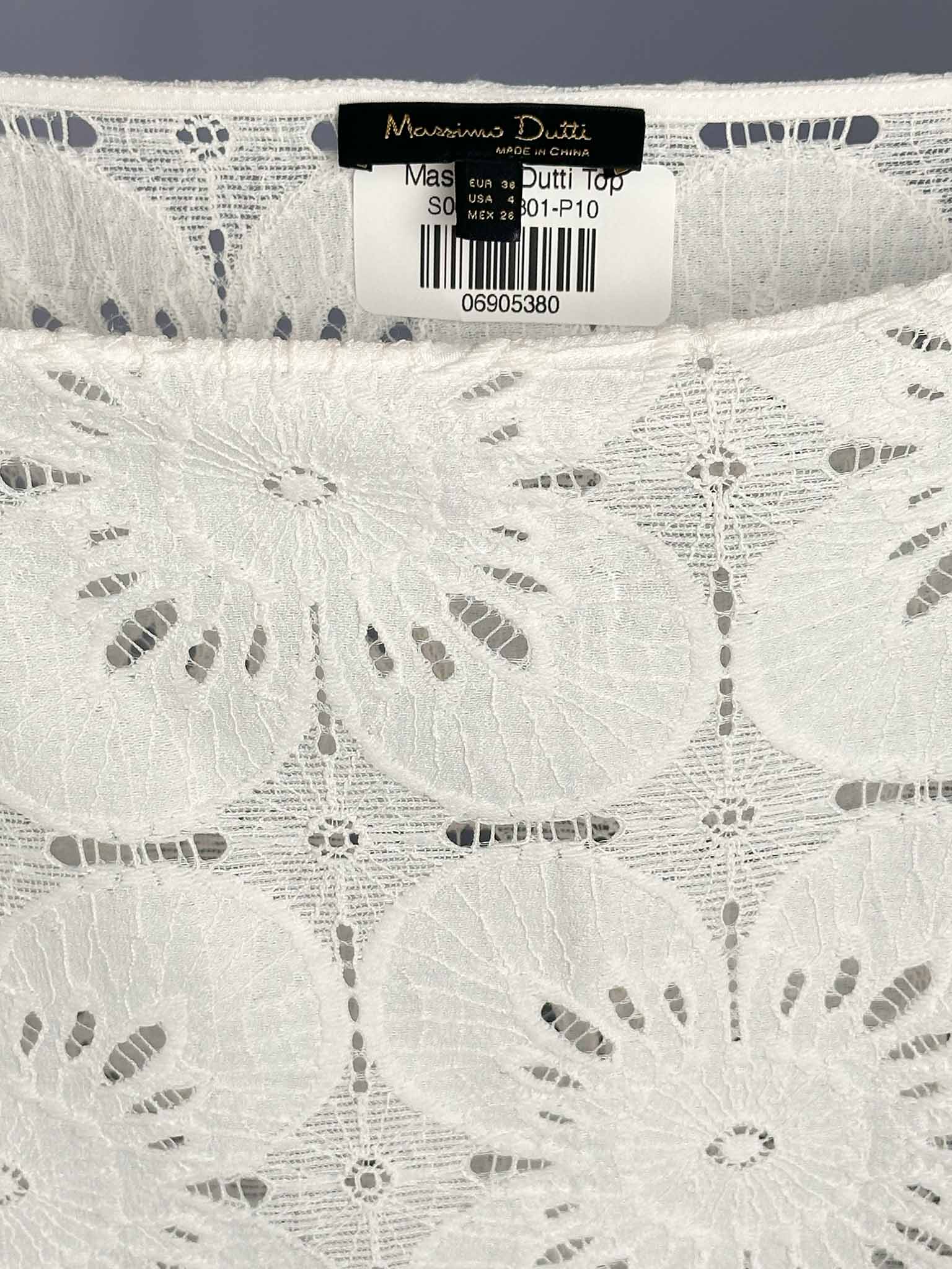 Close-up of a lace fabric with a Massimo Dutti label on a gray background