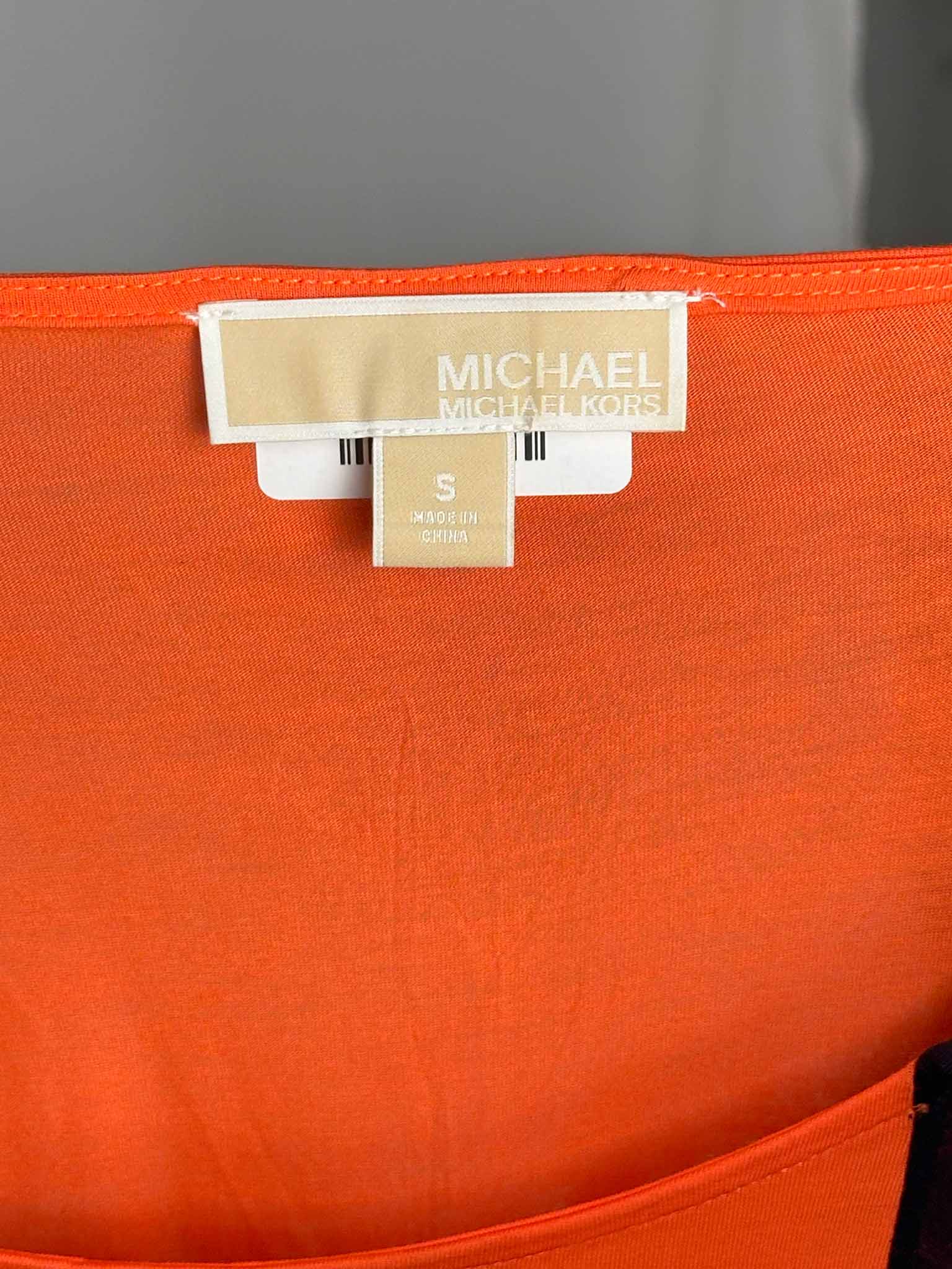 Close-up of an orange garment with a 'Michael Kors' label on a gray background