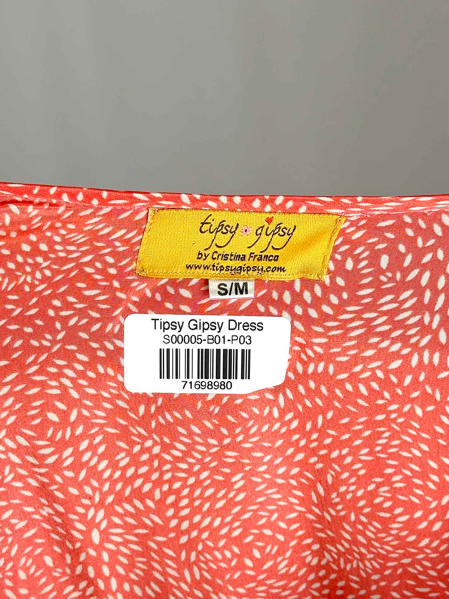 Close-up of a 'Tipsy Gipsy' dress label on a pink fabric with white patterns.