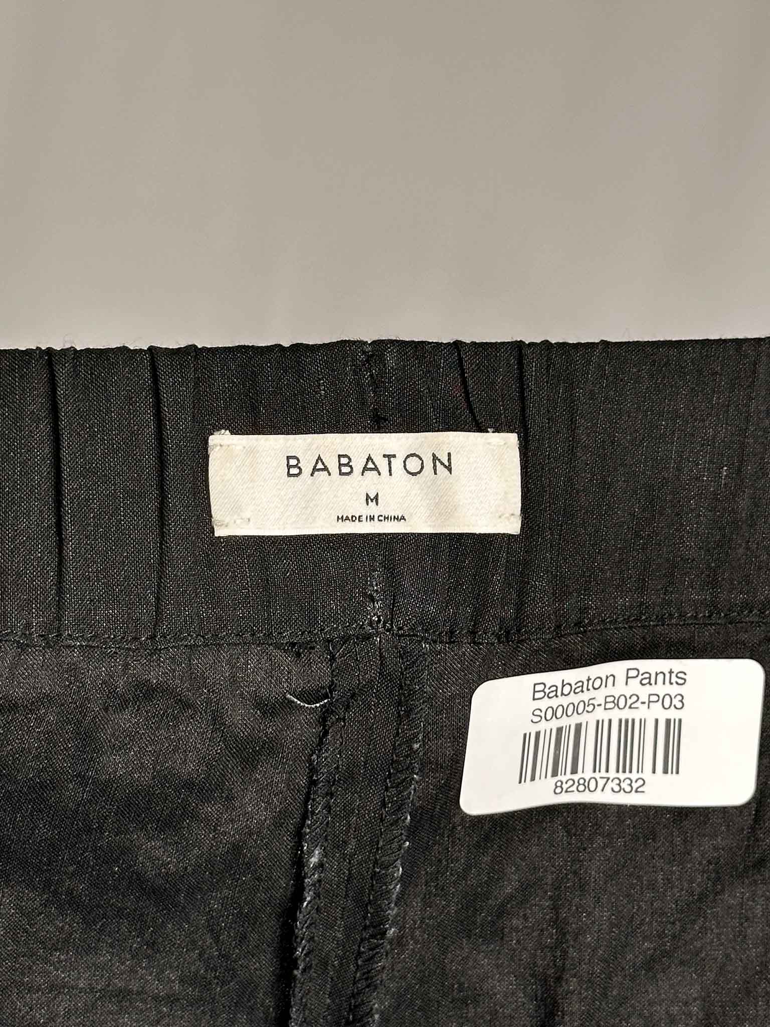 Close-up of black pants with Babaton label and barcode on a gray background
