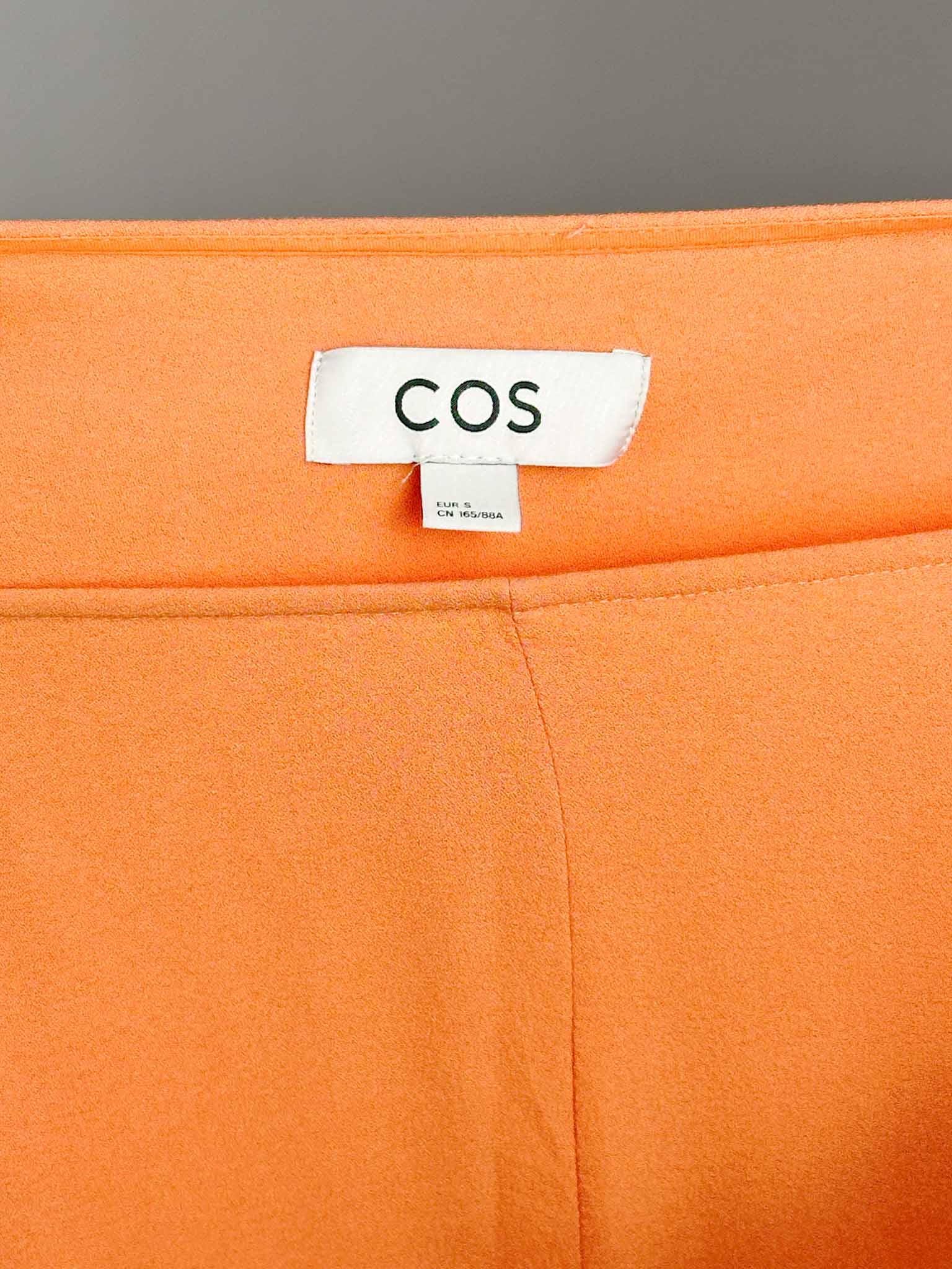Close-up of an orange fabric with a COS label on a gray background