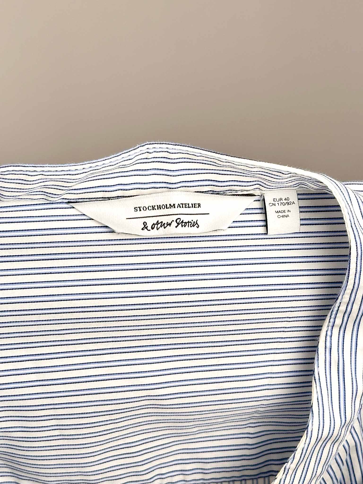 Close-up of a striped shirt with & Other Stories brand labels on a neutral background