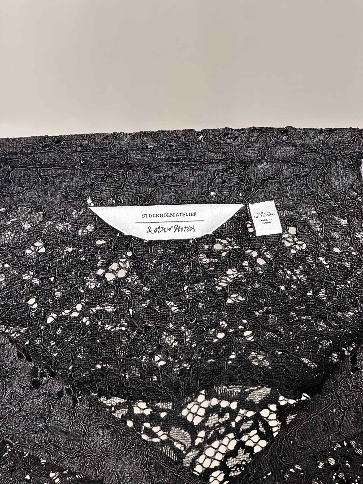 Black lace fabric with a & Other Stories brand label on a gray background