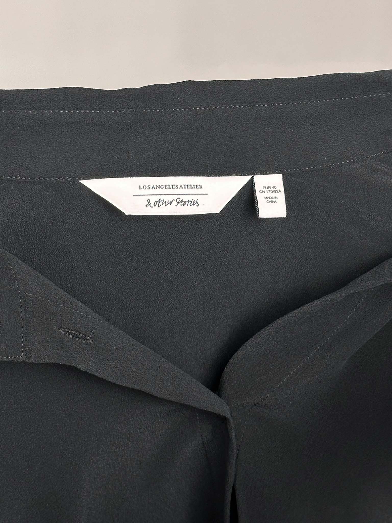 Dark fabric with a & Other Stories brand label on a beige background